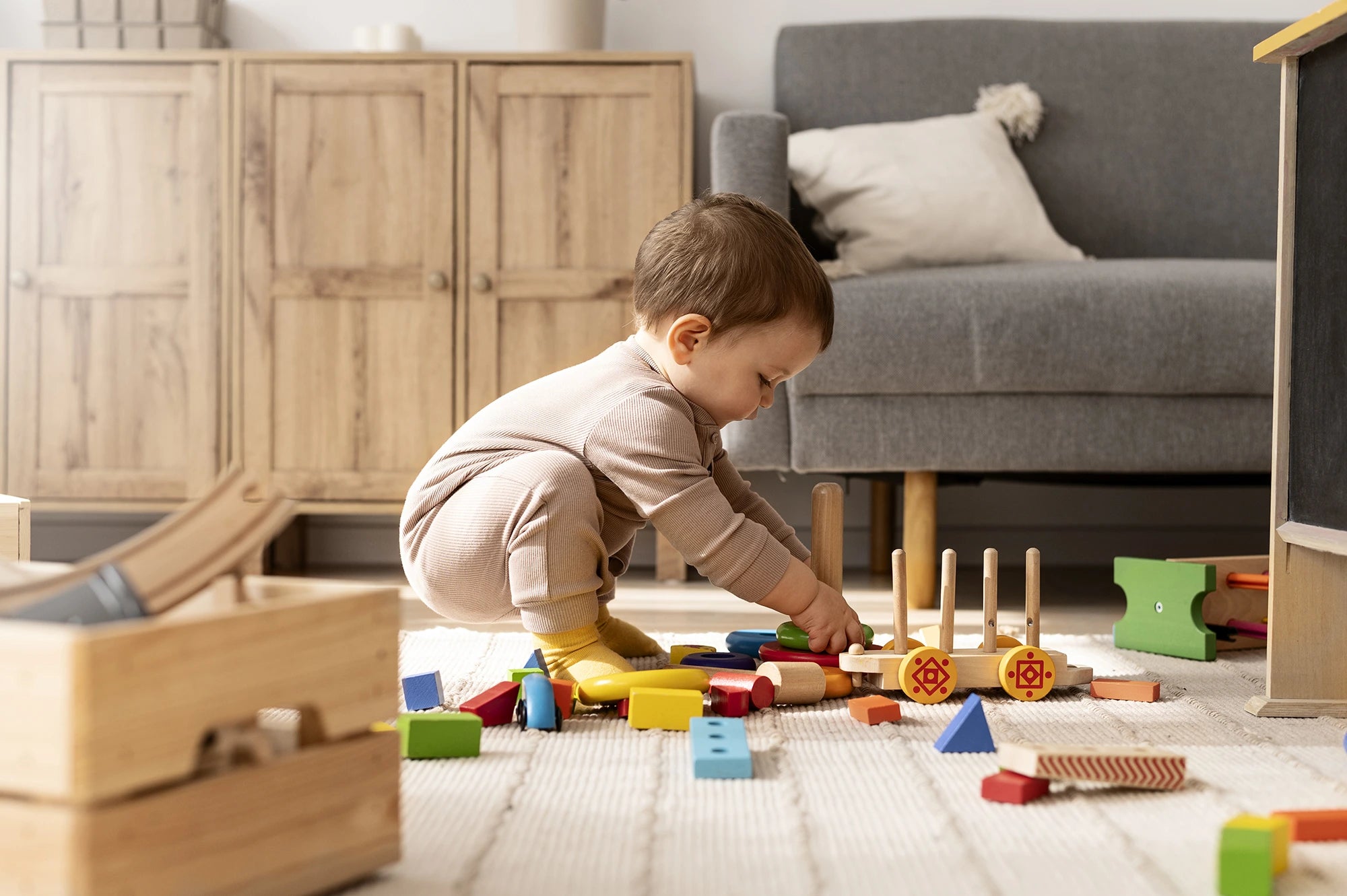 Child playing with toys on a carpeted floor in a room with wooden furniture and a gray sofa.
