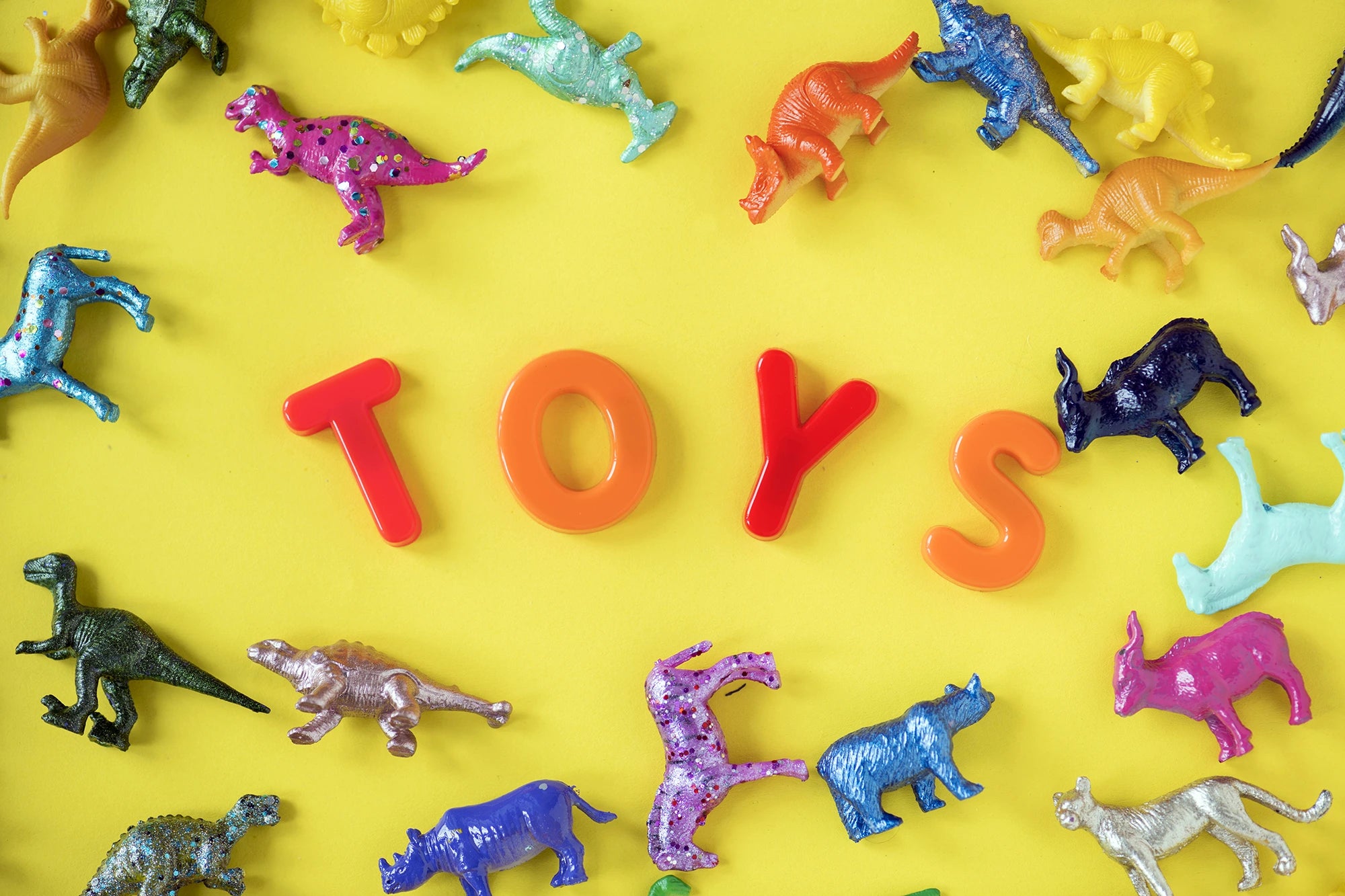 Colorful toy dinosaurs arranged around the word 'TOYS' on a yellow background